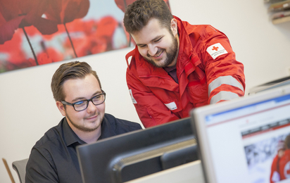 EDV - © Österreichisches Rotes Kreuz Markus Hechenberger Ein Zivildiener sitzt am Schreibtisch und wird durch einen Rotkreuz Mitarbeiter in die EDV eingeschult