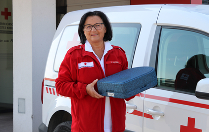 Essen auf Rädern - © OÖRK / Affenzeller Eine Frau hält eine Essensbox in der Hand und steht vor einem Rotkreuz-Auto