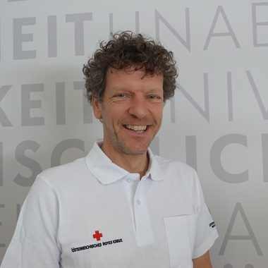 Martin Rettenbacher - © Rotes Kreuz Tirol Christine Widmann Martin Rettenbacher im Portrait im weißen Polo vor Grundsätzewand