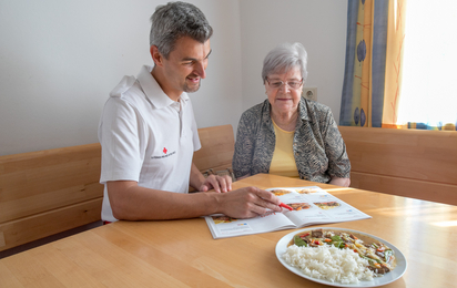 Zuhause Essen vom Roten Kreuz Niederösterreich - © RK NÖ/Lukas Hürner Ein Rotkreuz-Mitarbeiter berät seine Kundin über die Speisenauswahl bei Zuhause Essen.