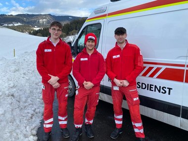 Drei Rettungssanitäter vor Rotkreuz Auto 