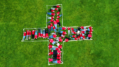 Jugendrotkreuzkinder liegen im Gras und bilden die Form des Roten Kreuzes