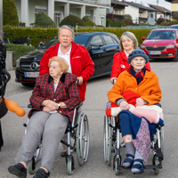 zwei ältere Damen werden von zwei Rotkreuz-Mitarbeiterinnen in einem Rollstuhl geschoben