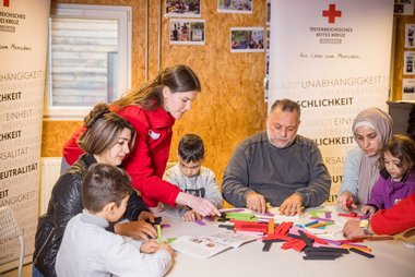 Eine Migrationsmitarbeiterin spielt mit Bausteinen mit Bewohner:innen des Rotkreuz-Asylquartiers