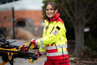 Eine Rettungssanitäterin in gelber Uniform schiebt die Trage zurück in den Rettungswagen.