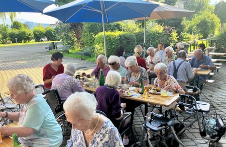 Bewohnerinnen und Bewohner sitzen an Tischen und genießen Essen und Getränke während des Grillfestes