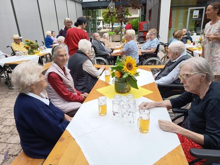 Bewohnerinnen des Seniorenwohnhauses an Tischen im Hof des Hauses
