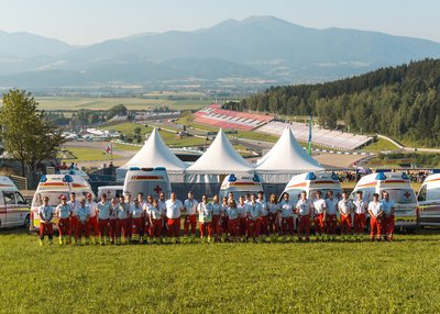 Einige Rotkreuz-Mitarbeiter:innen stehen in einer Gruppe zusammen. Im Hintergrund erkennt man den Red Bull Ring.