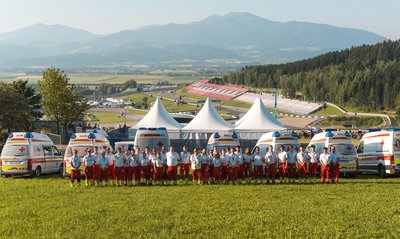 Einige Rotkreuz-Mitarbeiter:innen stehen in einer Gruppe zusammen. Im Hintergrund erkennt man den Red Bull Ring.
