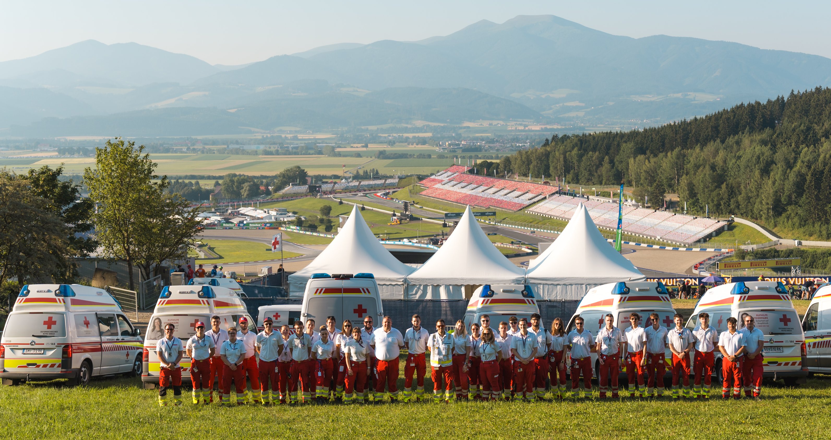 Einige Rotkreuz-Mitarbeiter:innen stehen in einer Gruppe zusammen. Im Hintergrund erkennt man den Red Bull Ring.