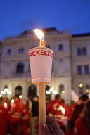 Eine Fackel im Fokus, dahinter unscharf Rotkreuzler:innen.