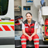 Eine Frau, die ein Freiwilliges Sozialjahr absolviert, sitzt auf den Stufen einer Rettungswagen
