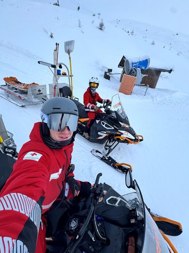 Zwei Rotkreuz-Sanitäter mit Skihelm auf Skidoos der Pistenrettung. Im Hintergrund ist eine Winterlandschaft im Skigebiet Wildkogel zu sehen.