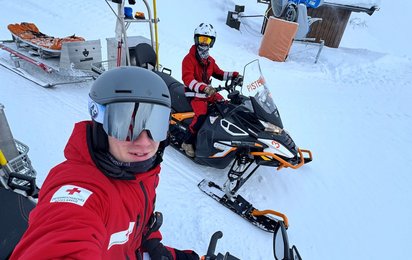 Zwei Rotkreuz-Sanitäter mit Skihelm auf Skidoos der Pistenrettung. Im Hintergrund ist eine Winterlandschaft im Skigebiet Wildkogel zu sehen.