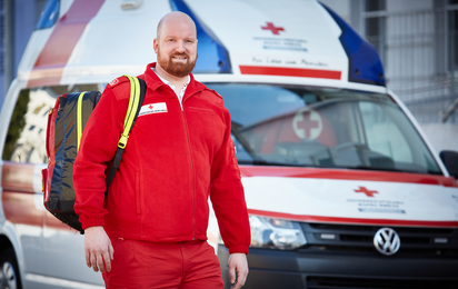 Ein männlicher Rettungssanitäter, steht vor einem Rettungsauto mit einem Rucksack über die Schulter.