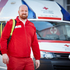 Ein männlicher Rettungssanitäter, steht vor einem Rettungsauto mit einem Rucksack über die Schulter.