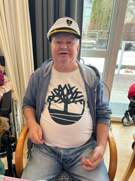 Ein Bewohner mit Kapitänsmütze sitzt an einem Tisch.