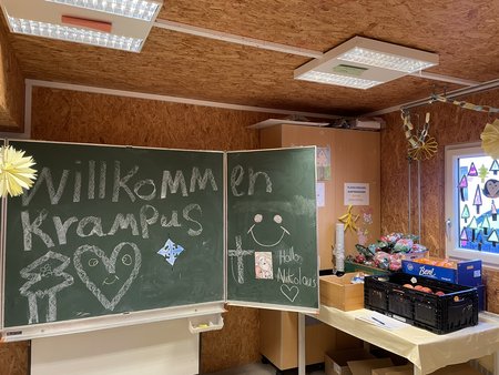 Schultafel in einem Aufenthaltsraum des Asylquartiers Flussbauhof. Darauf steht in Kreide geschrieben: "Willkommen Krampus" und "Hall Nikolaus", jeweils mit einem Herz versehen.