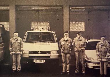 Hofinnenansicht der Bezirksstelle mit den alten Garagen, drei Fahrzeugen und dazugehörigen Personal in der Frontalansicht.