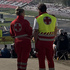 Zwei Rotkreuz-Mitarbeiter:innen stehen in Uniform am Red Bull Ring und überblicken das Geschehen auf den Tribünen und der Rennstrecke.