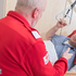 Ein Rotkreuz-Mitarbeiter erklärt einem im Bett liegenden Patienten die Fernsteuerung des Pflegebettes.