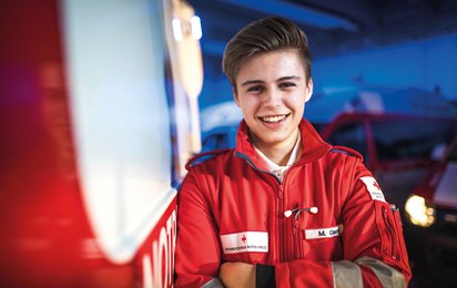 © ÖRK/Florian Schodritz Ein junger Freiwilliger im Rettungsdienst steht vor einem Rettungsauto und lächelt