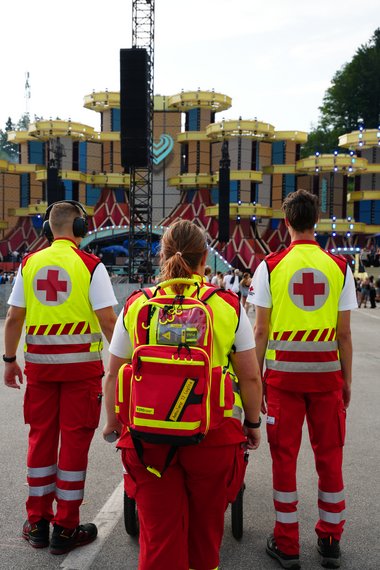 3 Rotkreuz-Helfer:innen stehen mit dem Rücken zu einer Bühne beim Electric Love Festival 2025