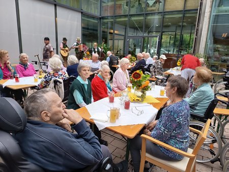 Bewohnerinnen des Seniorenwohnhauses an Tischen im Hof des Hauses