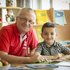ein Freiwilliger unterstützt ein Kind beim Lesen, beide lächeln in die Kamera
