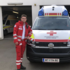 Kosovar Hoti steht in Rotkreuz-Uniform schräg vor einem Rettungswagen und lehnt sich leicht mit seinem linken Arm an der Motorhaube an.