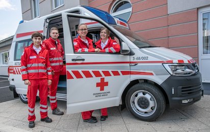 Gruppenfoto junger Menschen vor einem Rotkreuz-Auto