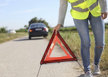Person mit Warndreieck vor PKW