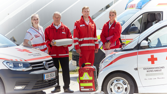 Vertreter_innen von Team Österreich, Essen auf Rädern, Rettungsdienst und Mobile Dienste vor den Autos