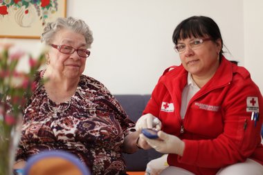 Eine Rotkreuz-Mitarbeiterin misst im Rahmen der Hauskrankenpflege bei einer Klientin den Blutzucker.