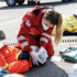 Eine Rotkreuz-Sanitäterin legt einer verletzten Person einen Kopfverband an.