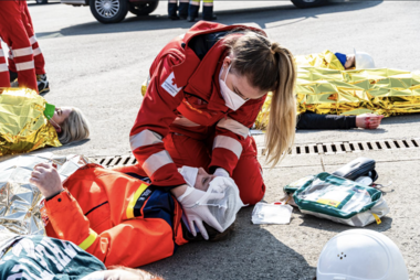 Eine Rotkreuz-Sanitäterin legt einer verletzten Person einen Kopfverband an.