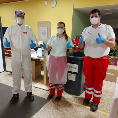 3 Mitarbeiter_innen mit Schutzausrüstung in einer Coronavirus-Teststrasse