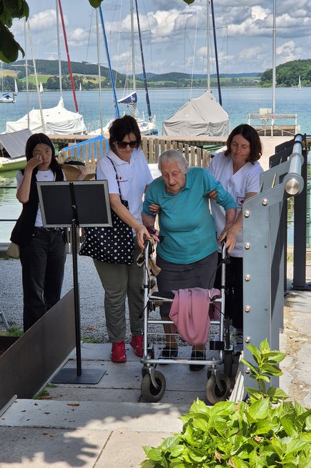 Mitarbeiterinnen helfen Bewohnerin auf dem Weg zum Seewirt am Mattsee.