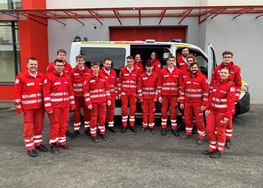 Ein Teamfoto aus dem Jahr 2023 im Innenhof vor und in einem Krankentransportwagen.