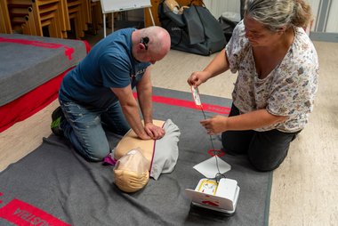 Zwei Menschen üben die Wiederbelebung mit Herzdruckmassage und Defibrillator an einer Übungspuppe.