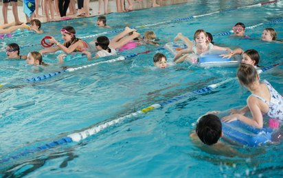 Mehrere Kinder in einem Schwimmbecken, teils auf Luftmatrazen, teils im Wasser.