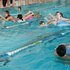 Mehrere Kinder in einem Schwimmbecken, teils auf Luftmatrazen, teils im Wasser.