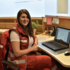 Michaela Scheiber sitzt in Rotkreuz-Uniform in einem Büro vor ihrem Notebook.