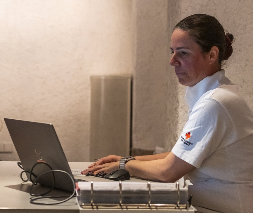 eine Ärztin im Rotkreuz Polo sitzt vor ihrem Laptop