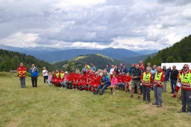 Rotkreuz-Mitarbeiter:innen und Gäste bei der Bergmesse, auf Bänken sitzend und stehend, mit Bergen im Hintergrund