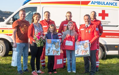 Gruppenfoto der Familie und Rotkreuz-Mitarbeitenden bei der Geschenkübergabe vor dem Rettungsauto