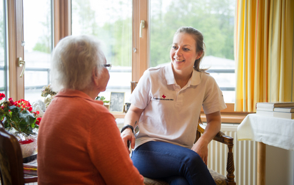Eine Pflege-Mitarbeiterin im Gespräch mit einer Bewohnerin eines Seniorenwohnhauses