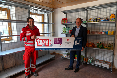 Im Bild ist Michael Volderauer vom Roten Kreuz und Rupert Sparber vom Gerätewerk Matrei vor einem Regal der Team Österreich Tafel. Die beiden halten das Schild mit den Logos in den Händen