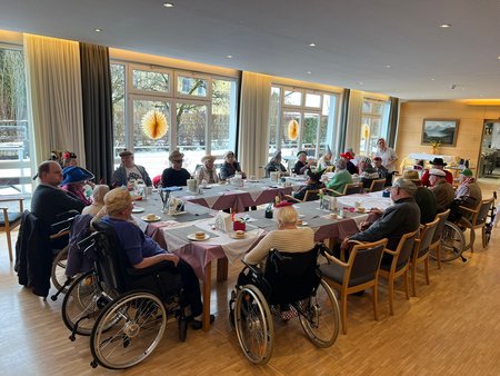 Die verkleideten Bewohnerinnen des Seniorenwohnhauses sitzen gemeinsam an einem großen Tisch und feiern Fasching.