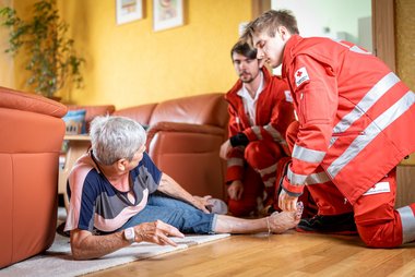 Rotkreuz-Sanitäter helfen einer Dame, nachdem sie auf ihrem Rufhillfe-Armband den Notrufknopf gedrückt hat.